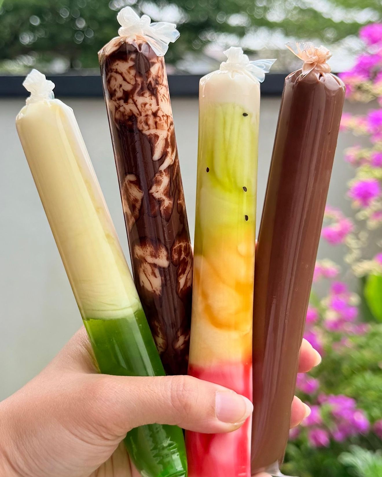 A hand holding four Aiskrim Twisty tubes in the garden